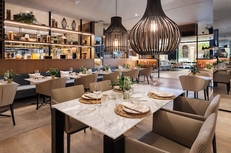 A modern restaurant interior with marble tables, wicker chairs, and pendant lighting.