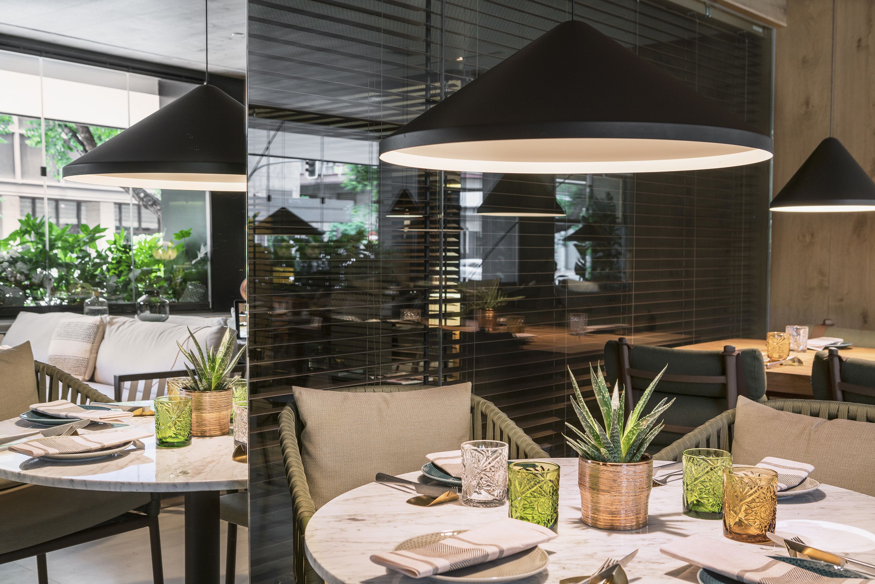 A modern dining area with round tables, green glassware, and woven plant pots.