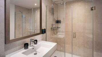 Un baño moderno con un espejo grande, un lavabo blanco y una zona de ducha con mampara de vidrio.