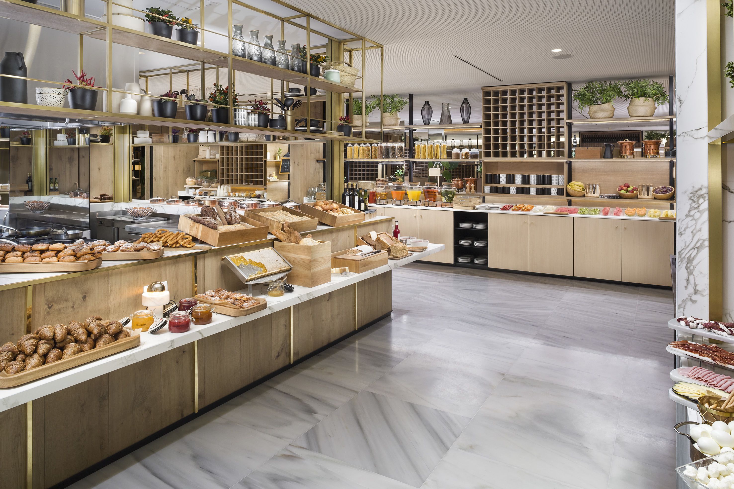 A modern kitchen with marble floors, wooden cabinetry, and various food items displayed on shelves and counters.