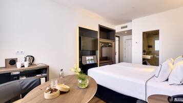 A modern hotel room with a bed, a desk, a chair, a small table with a vase, and a wardrobe.