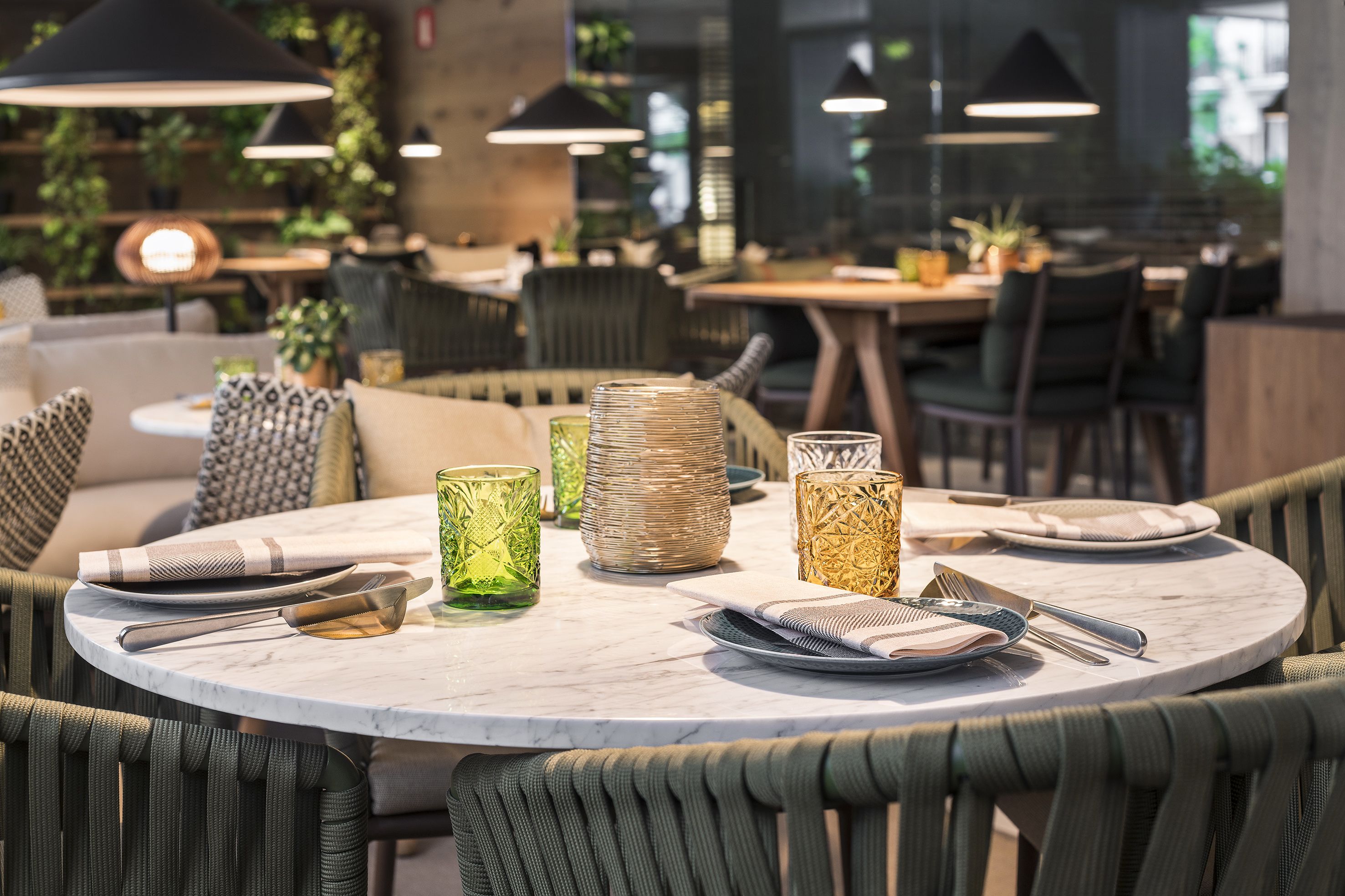 Une table de salle à manger ronde, surmontée d’un plateau en marbre, entourée de chaises recouvertes d’un tissu vert.