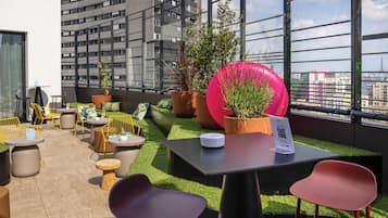 A rooftop terrace with outdoor seating, potted plants, and a view of the cityscape.
