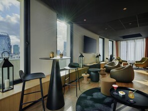 A modern hotel room with a city view, a round table, bar stools, a sofa, and a flat-screen TV. - Hotel Mercure Paris La Défense (Courbevoie)