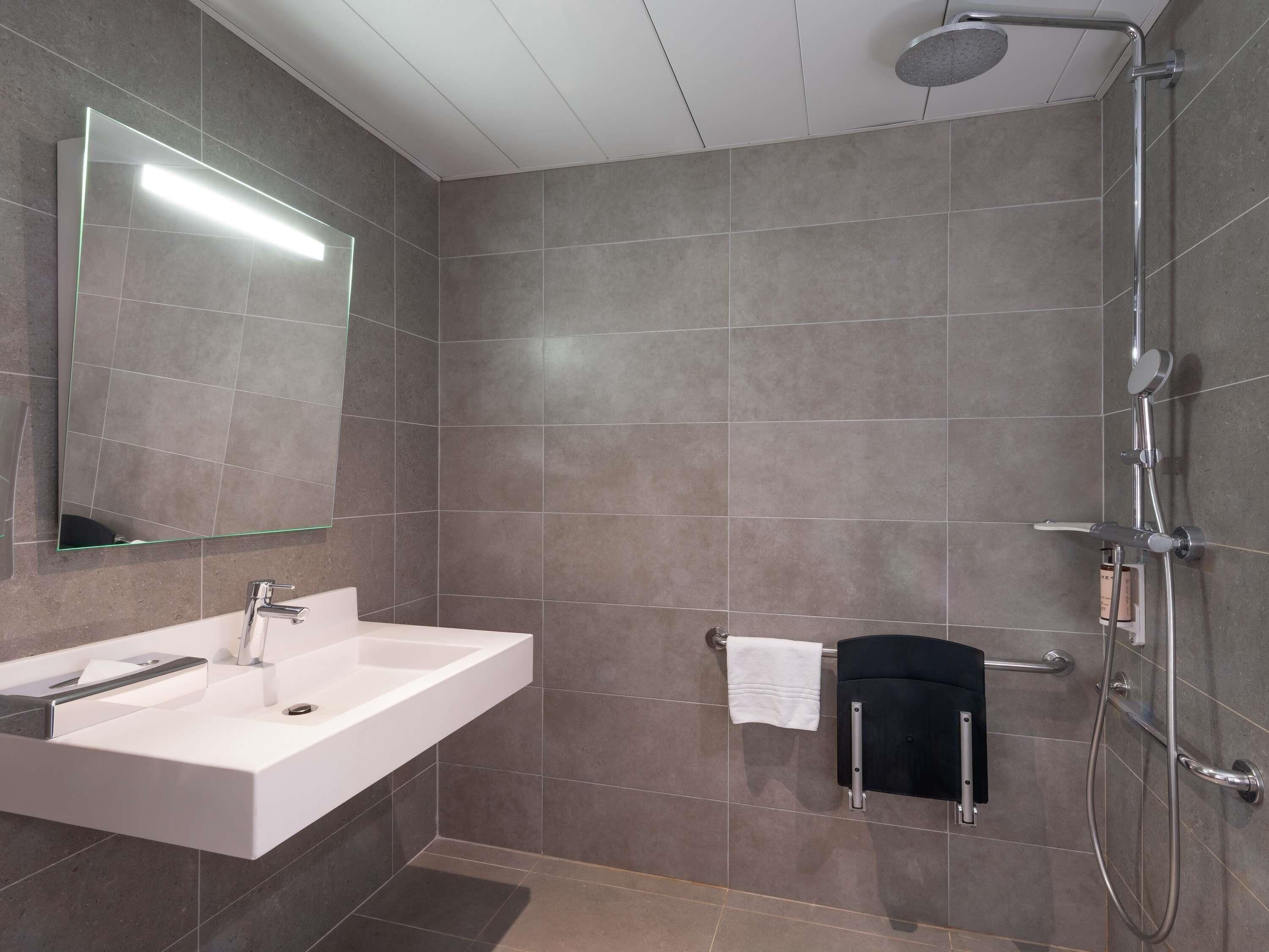 A modern bathroom with a large mirror, a white sink, a shower, and a towel rack.