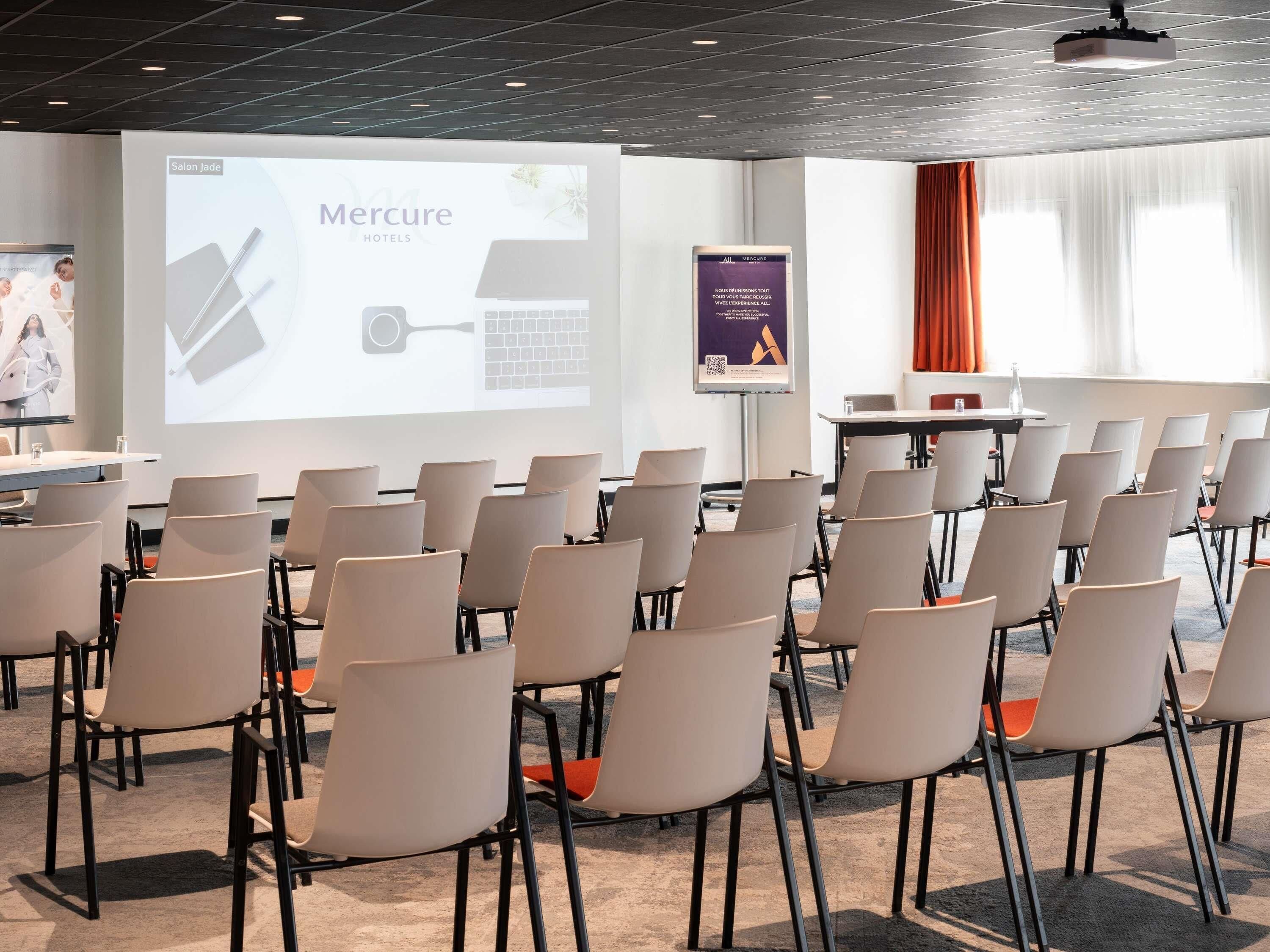 A conference room with rows of chairs, a presentation screen, and a banner for Mercure Hotels.