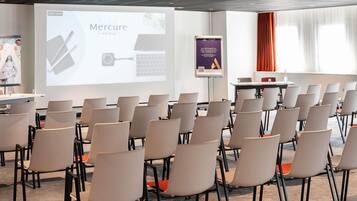 A conference room with rows of chairs, a presentation screen, and a banner for Mercure Hotels.