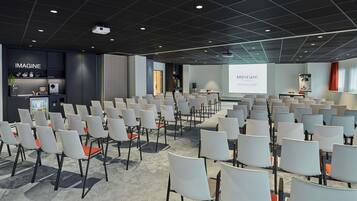 Un salón de conferencias con filas de sillas, una pantalla de proyector y una zona para presentaciones.
