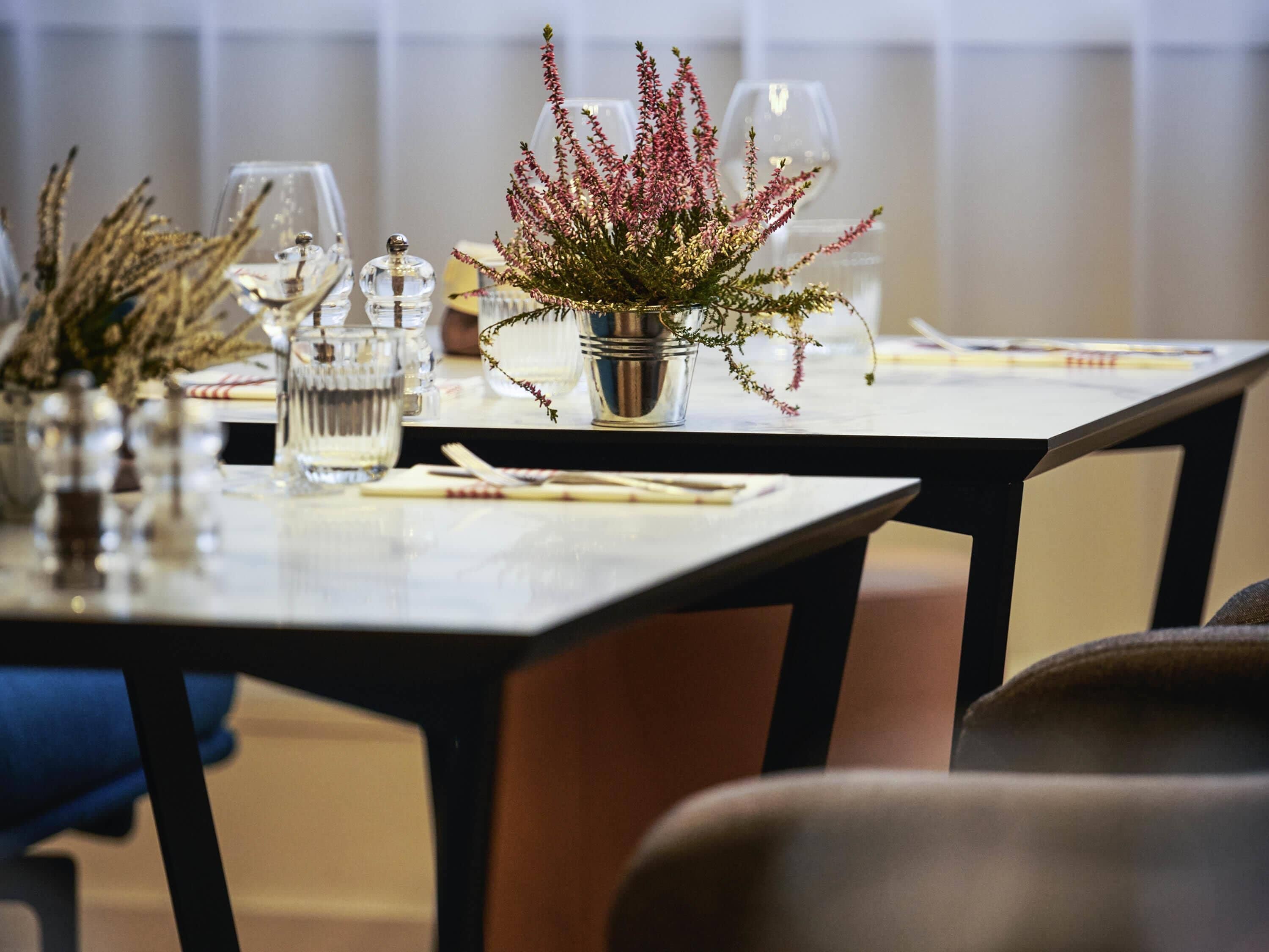 Une table dressée avec des verres transparents, un pichet en métal et une petite plante en pot.