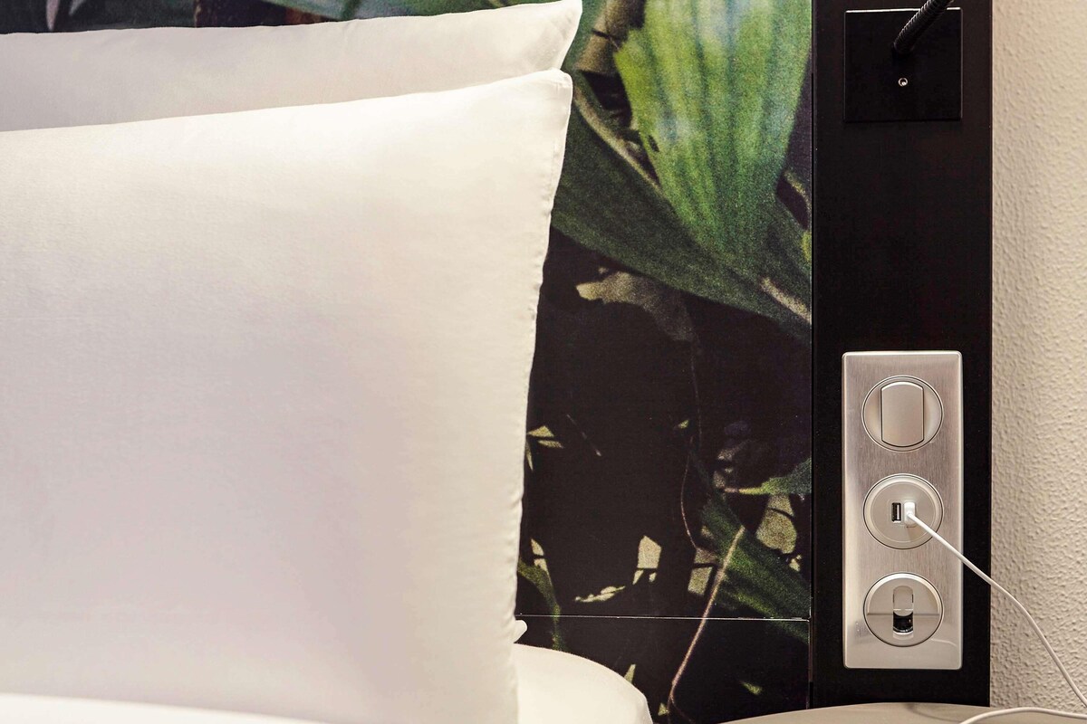 A bed with white sheets, a power outlet with a USB port, and a wall-mounted switch.