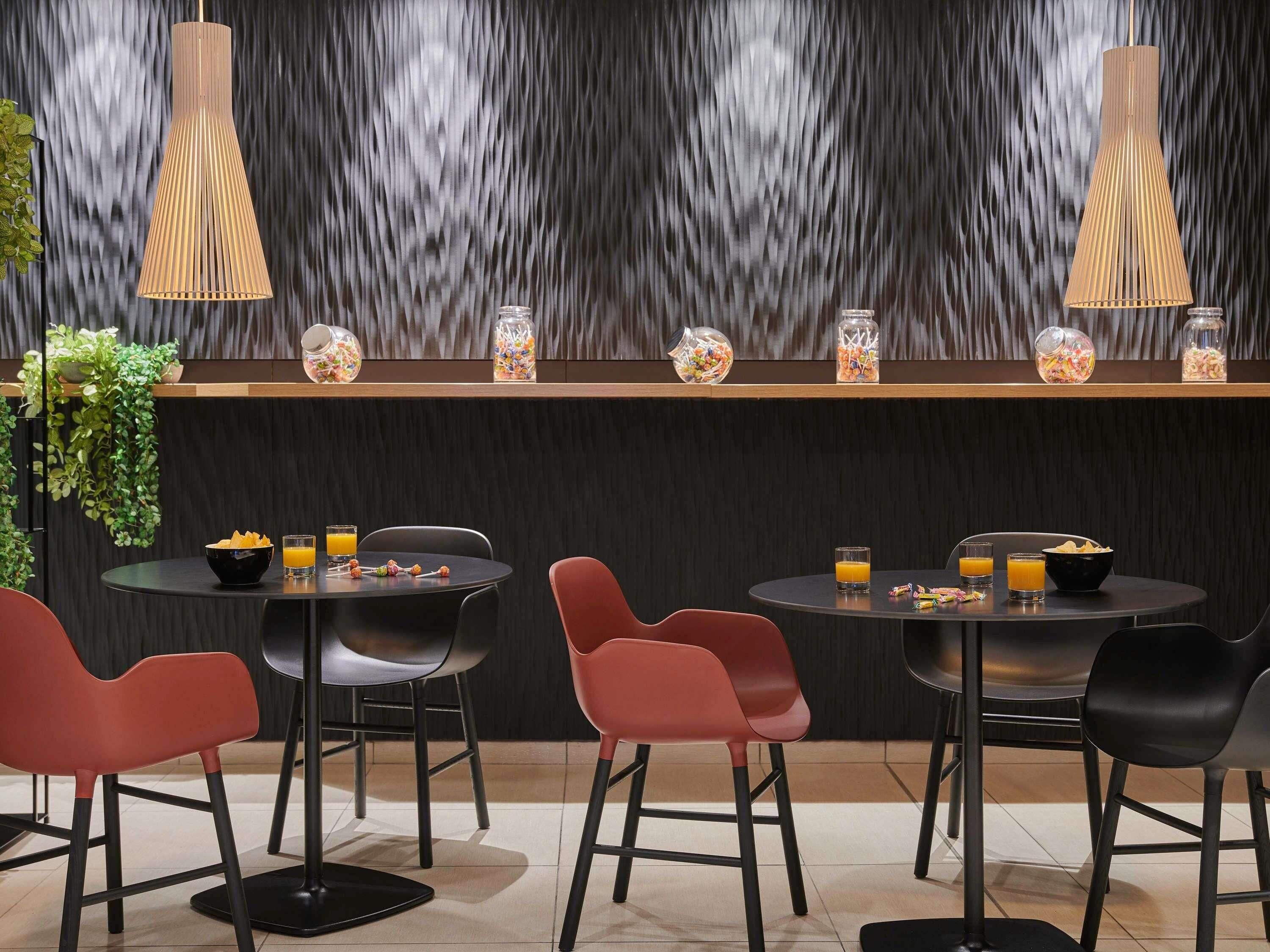 A modern dining area with round tables, red chairs, and two hanging pendant lights.
