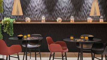A modern dining area with round tables, red chairs, and two hanging pendant lights.