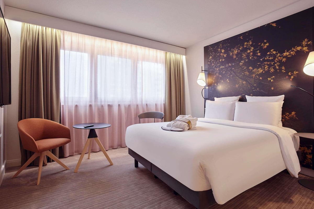 Ett hotellrum med en säng, en stol, ett litet bord och en vägg med ett lövmönster.