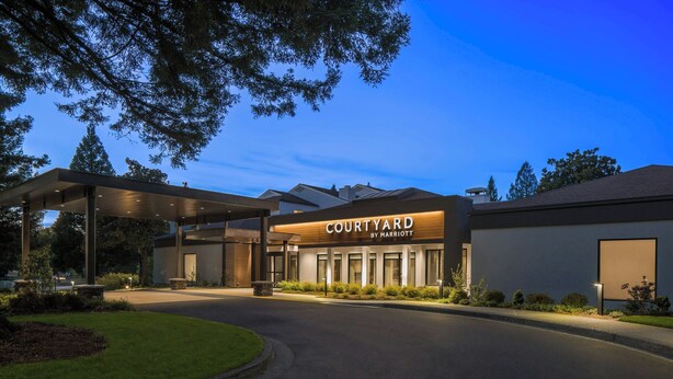 A modern hotel entrance with a covered driveway, well-maintained lawn, and a clear sky. - Courtyard by Marriott Portland Beaverton (Beaverton)