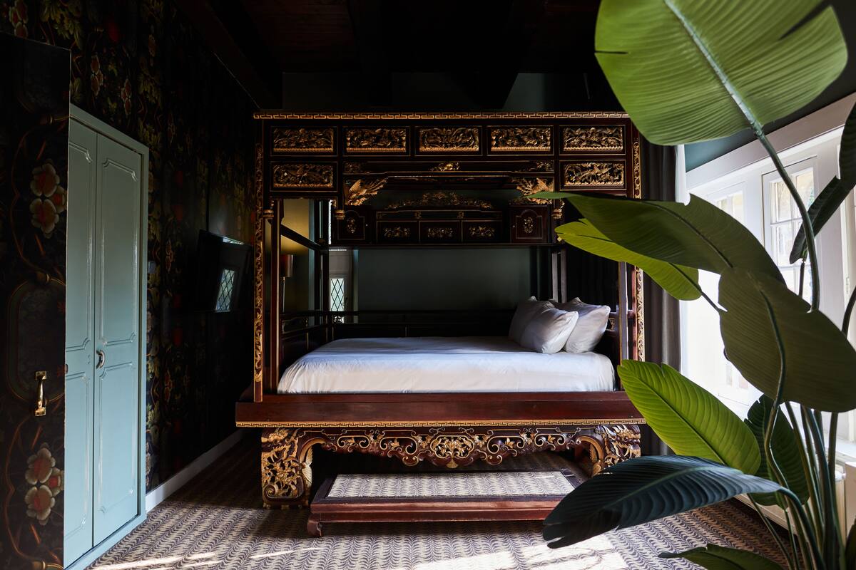 Una cama con dosel y tallas elaboradas, una planta grande y un suelo con diseño.