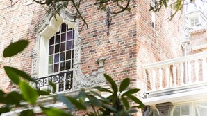 A brick building with a white balcony and a window with a decorative frame. - Kasteel Kerckebosch (Zeist)