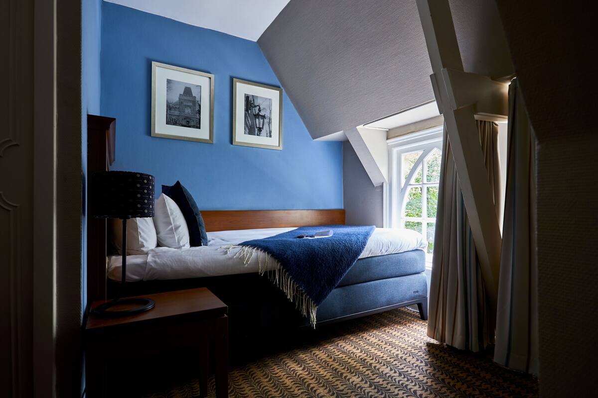 Un dormitorio con cama, mesita de noche, lámpara y dos cuadros en la pared.