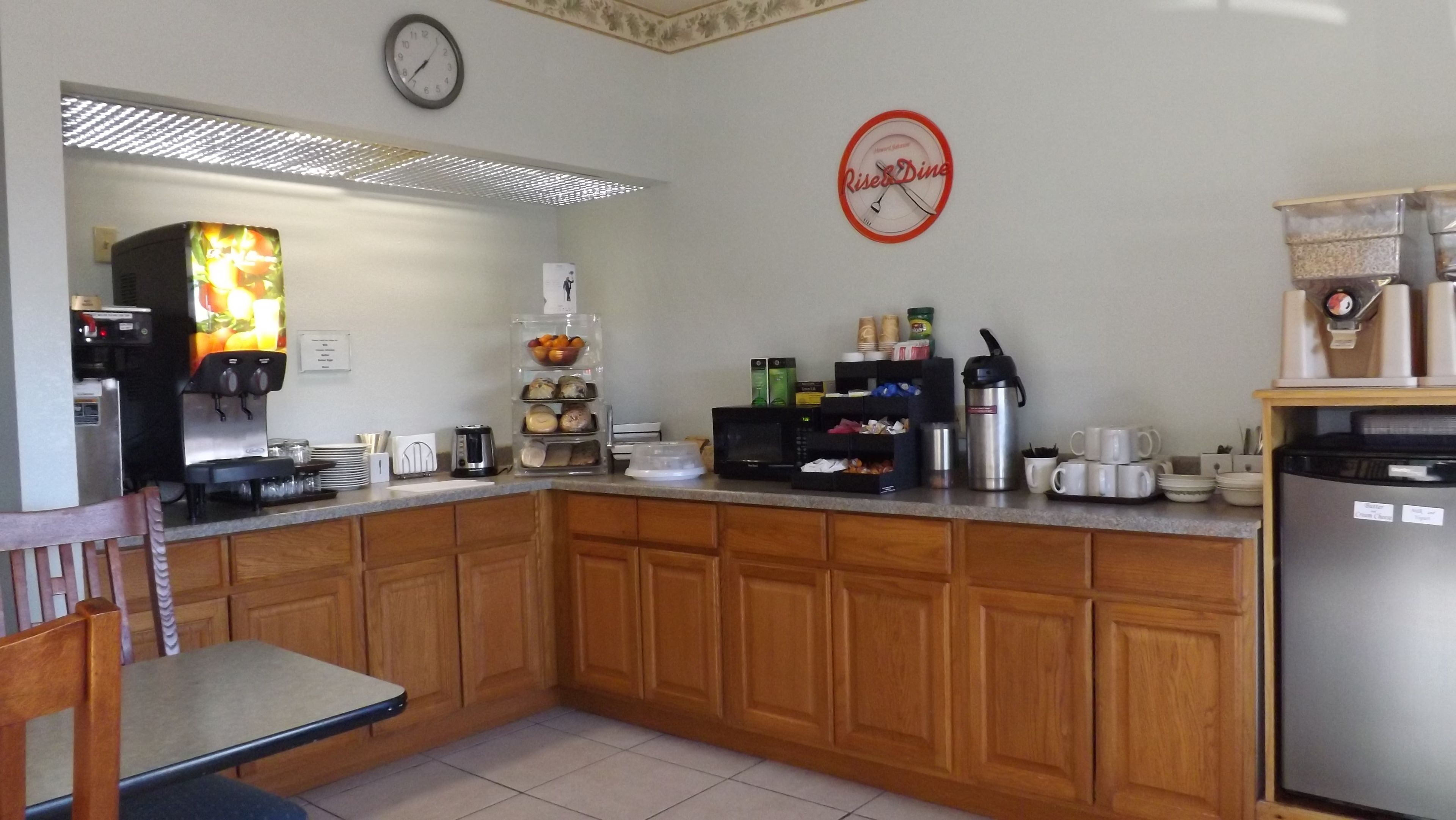 Una cucina con armadietti in legno, un frigorifero, un forno a microonde, una macchina da caffè e una sveglia appesa al muro.