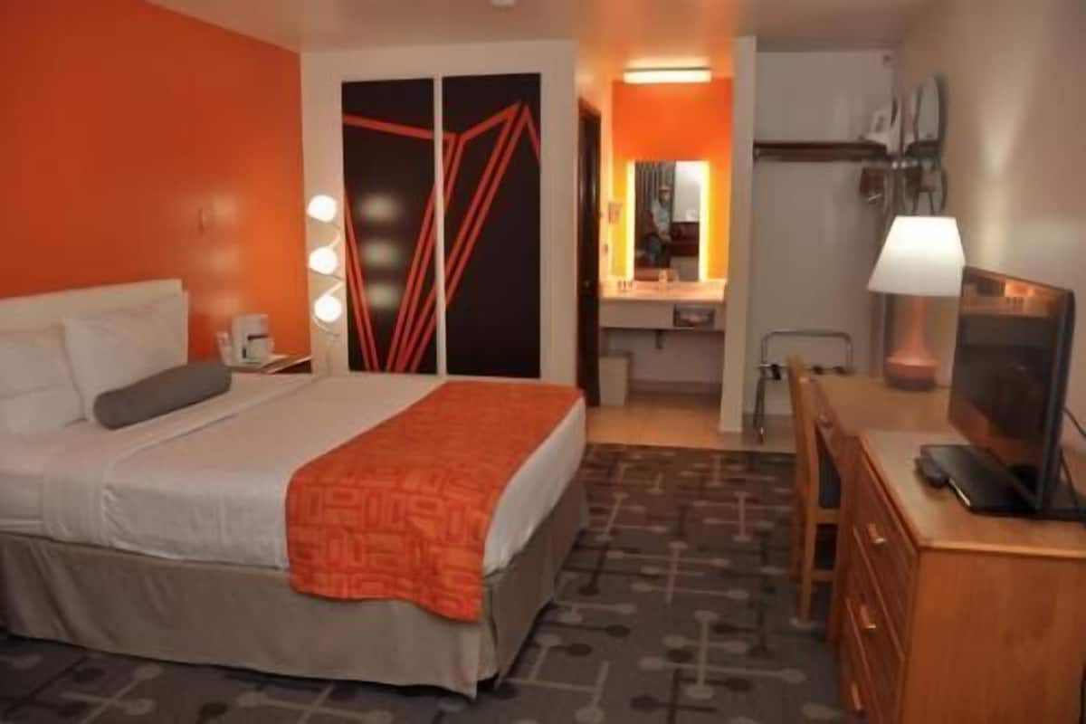 A hotel room with a bed, a desk, a chair, a TV, and a bathroom.