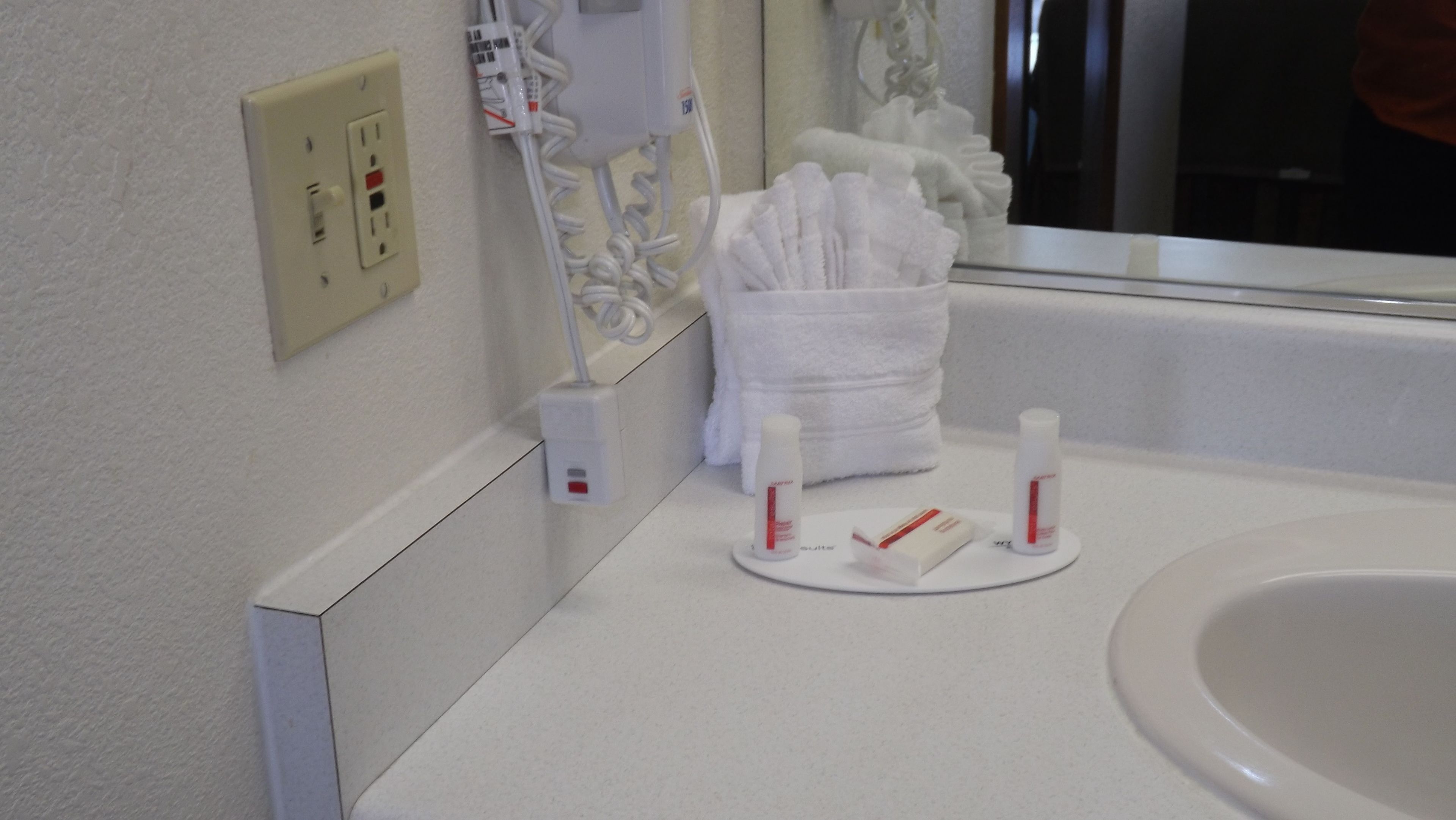 Une salle de bain avec un lavabo blanc, un porte-serviettes avec des serviettes pliées et des articles de toilette posés sur le comptoir.