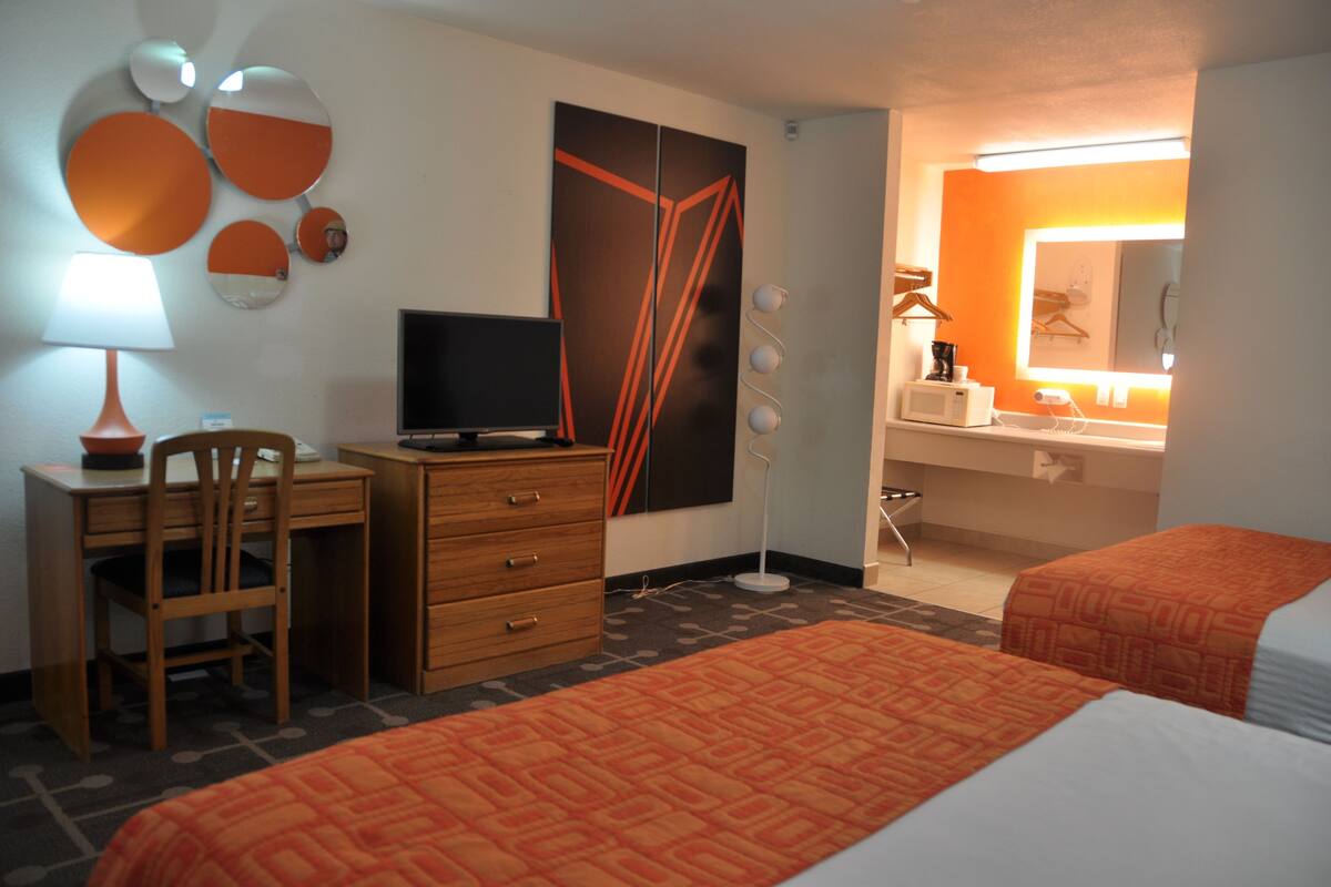Habitación de hotel con escritorio, silla, televisión, cama y baño con espejo y lavabo.