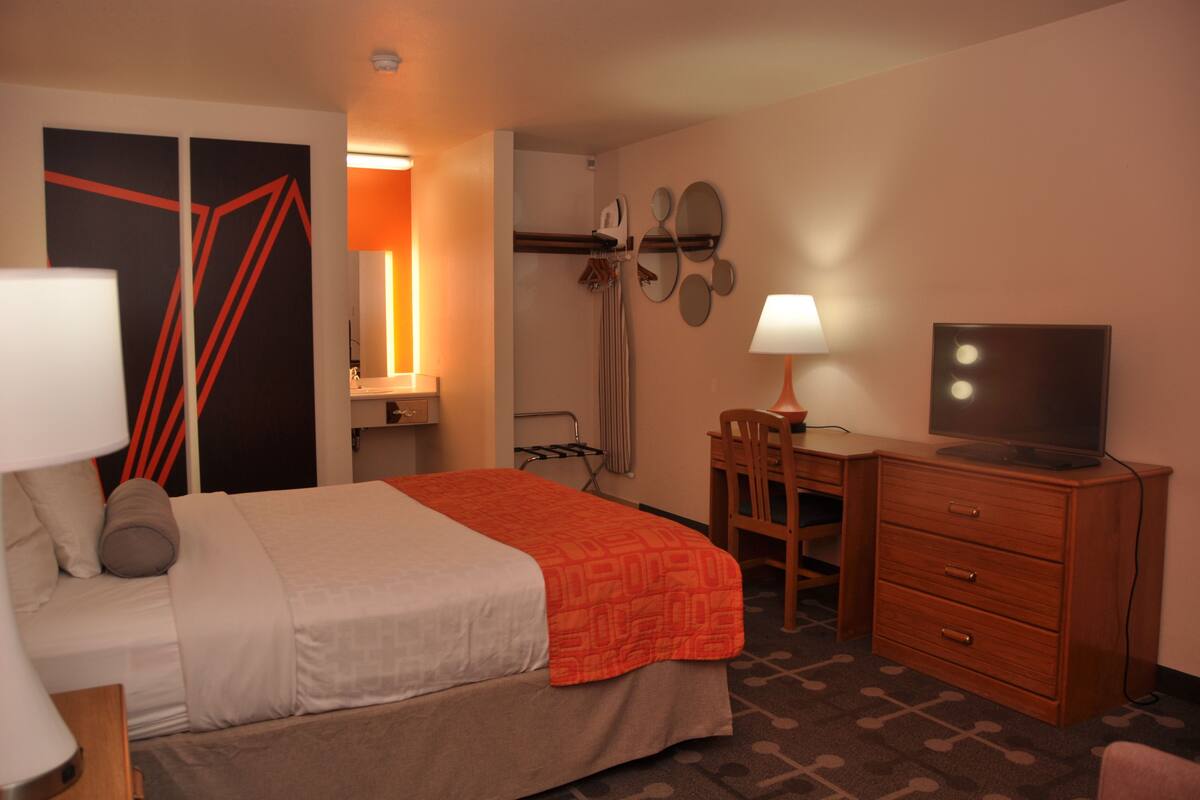 Habitación de hotel con cama, escritorio con silla, televisor, armario y baño con ducha y toallero.