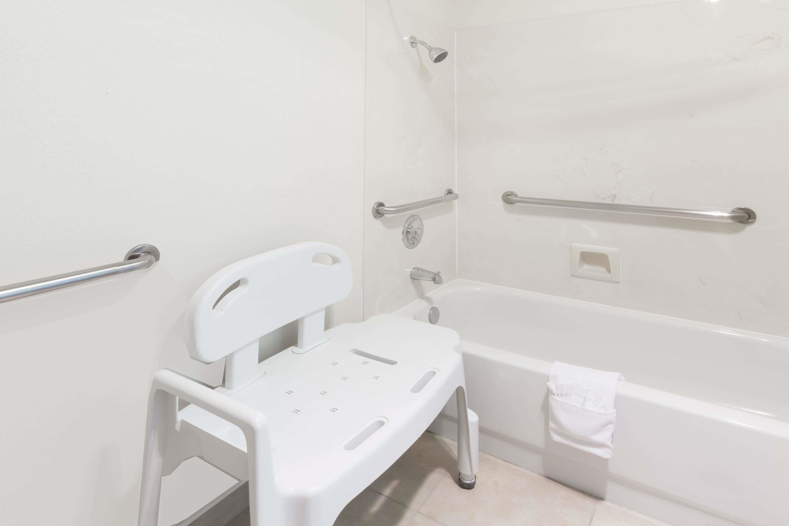 Un baño con una bañera blanca, ducha blanca y barra de apoyo blanca.