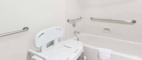 Un baño con una bañera blanca, ducha blanca y barra de apoyo blanca.