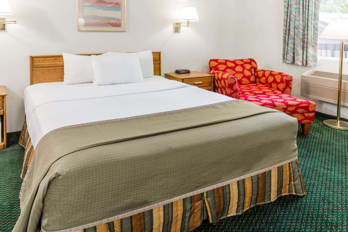 Una habitación de hotel con una cama grande, una silla, una mesita de noche y una lámpara de pared.