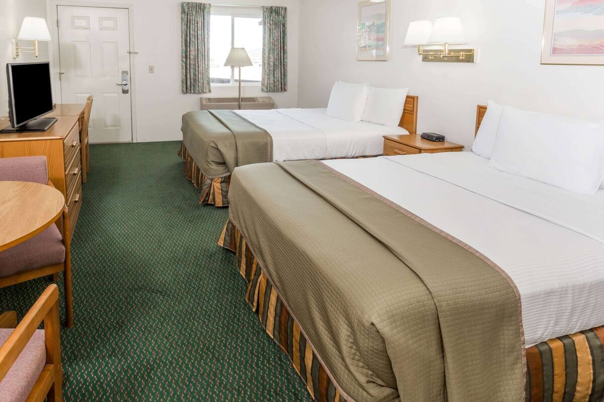 Habitación de hotel con dos camas, un escritorio con computadora, una silla y una ventana con cortinas.