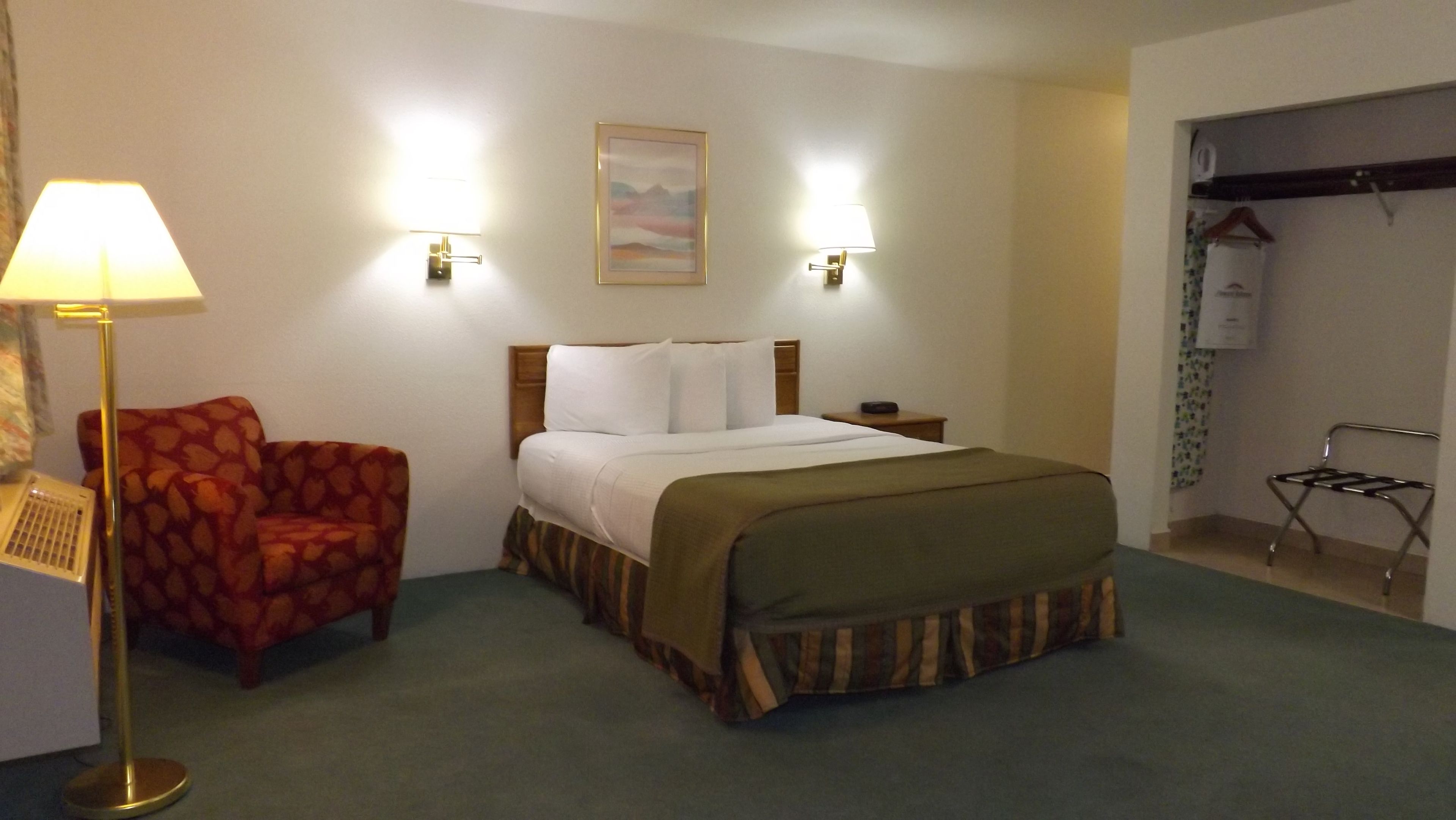 A hotel room with a bed, a chair, a lamp, and a painting on the wall.