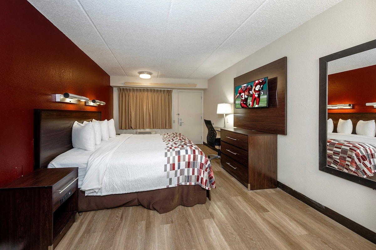 Habitación de hotel con una cama grande, un escritorio, una silla, un televisor y un espejo.