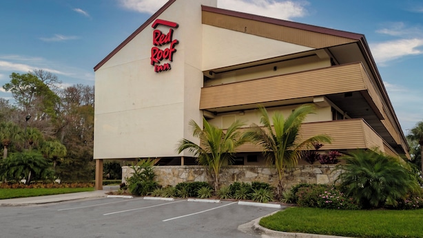 A Red Roof Inn with a modern architectural design, featuring a prominent red and black sign, a parking lot, and surrounding greenery. - Red Roof Inn Tampa - Brandon (Tampa)