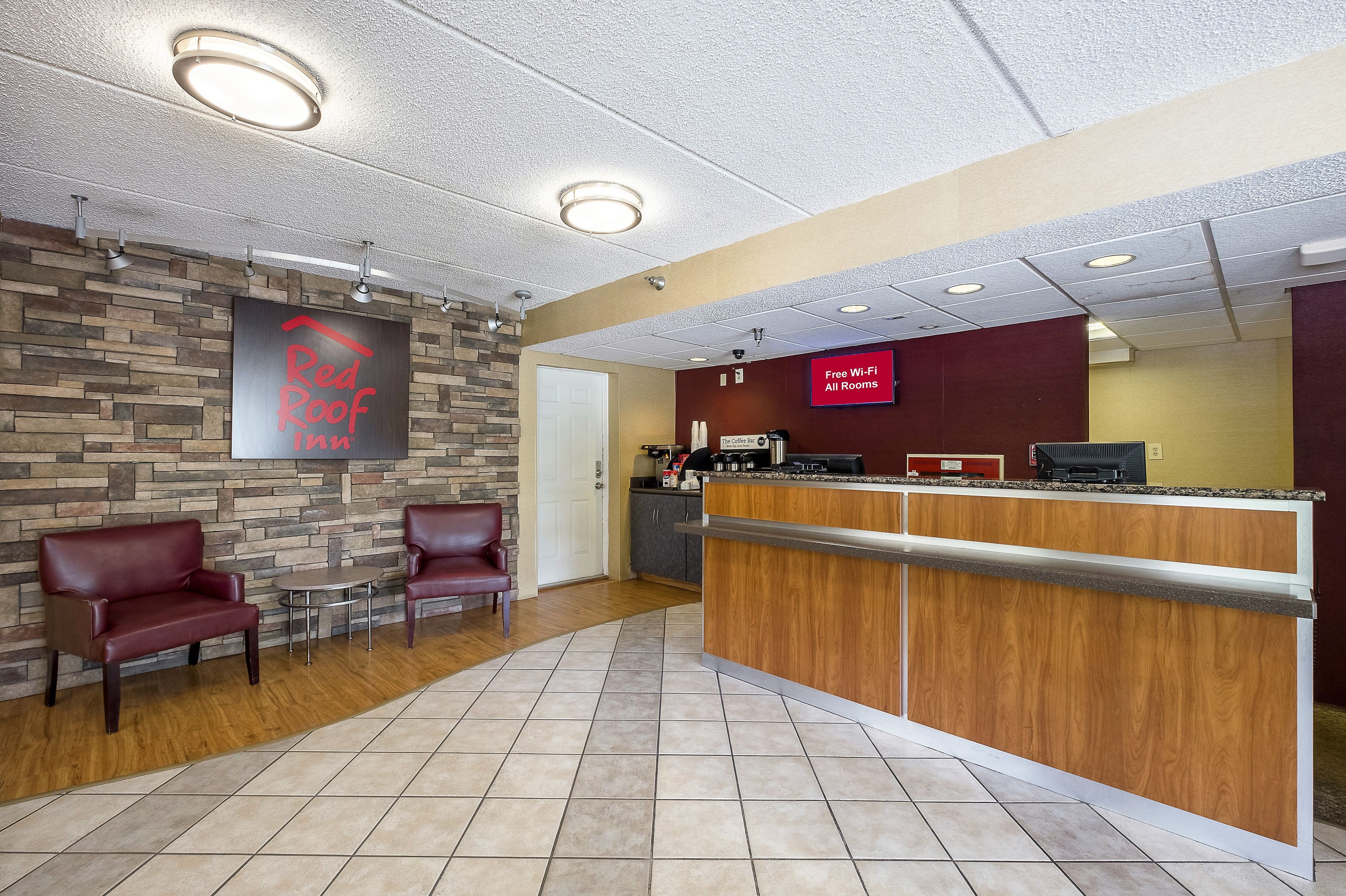 Zona d'entrada d'un Red Roof Inn, amb paret de pedra, seients de cuir, taulell de recepció de fusta i un cartell que indica Wi-Fi gratuït a totes les habitacions.