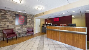 A Red Roof Inn reception area with a stone wall, leather chairs, a wooden reception desk, and a sign indicating free Wi-Fi in all rooms. - Red Roof Inn Tampa - Brandon (Tampa)