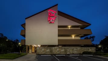 A Red Roof Inn with a modern architectural design, featuring a prominent neon sign, a parking lot, and a stone facade.