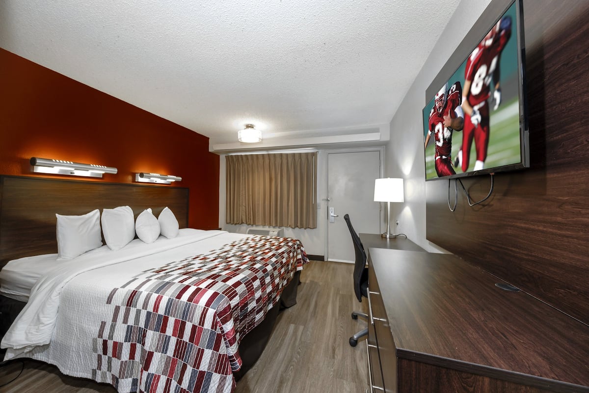 Una habitación de hotel con una cama grande, un escritorio, un televisor montado en la pared y una ventana con cortinas.