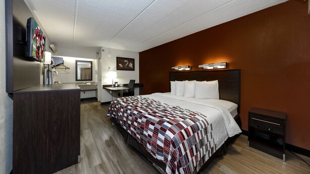 A hotel room with a bed, a desk, a chair, a TV, and a minibar. - Red Roof Inn Tampa - Brandon (Tampa)