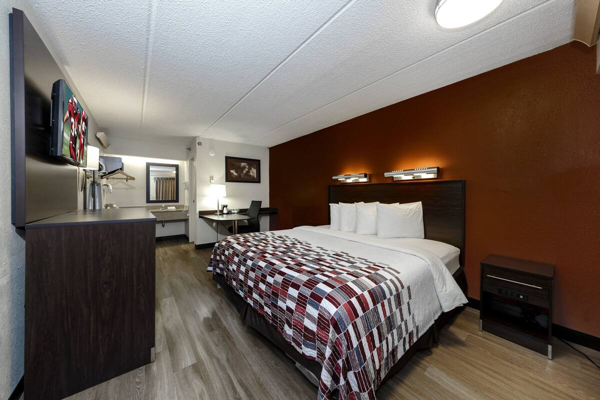 A hotel room with a bed, a desk, a chair, a TV, and a minibar.