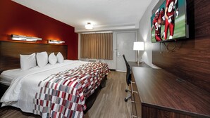 A hotel room with a bed, a desk, a TV, and a window with curtains. - Red Roof Inn Tampa - Brandon (Tampa)