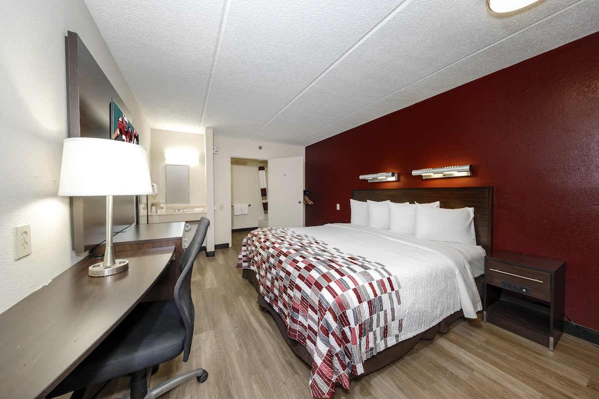 A hotel room with a bed, desk, chair, and a nightstand.