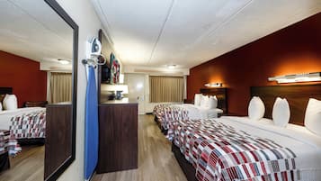 A hotel room with a mirrored wall, a desk with a lamp, a bed with a checkered bedspread, and a headboard with a light fixture.