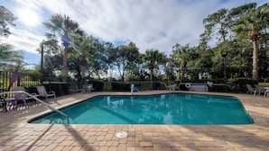 A rectangular swimming pool with a brick deck, surrounded by a metal fence and trees. - Red Roof Inn Tampa - Brandon (Tampa)