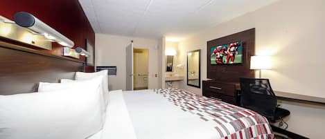 Habitación de hotel con una cama grande, un escritorio, una silla, un televisor y un baño visible a través de una puerta abierta.