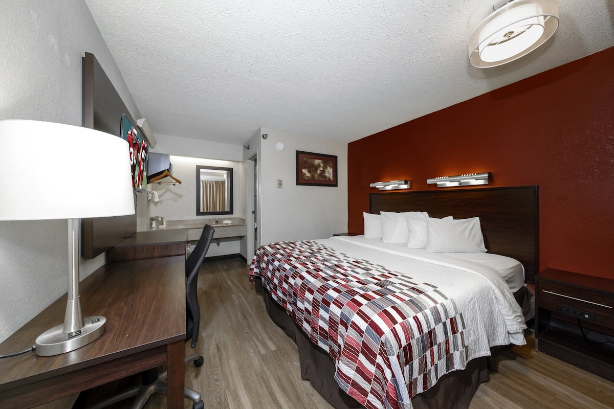 A hotel room with a bed, desk, chair, lamp, and a mirror.