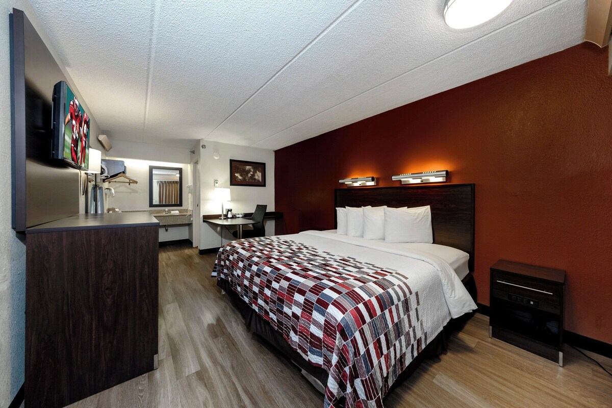 Ein Hotelzimmer mit Bett, Nachttisch, Schreibtisch, Stuhl und einem an der Wand befestigten Fernseher.