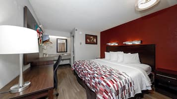 A hotel room with a bed, desk, chair, and a mirror.