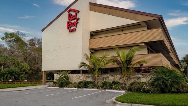A Red Roof Inn with a modern architectural design, featuring a prominent red and black sign, a parking lot, and surrounding greenery. - Red Roof Inn Tampa - Brandon (Tampa)