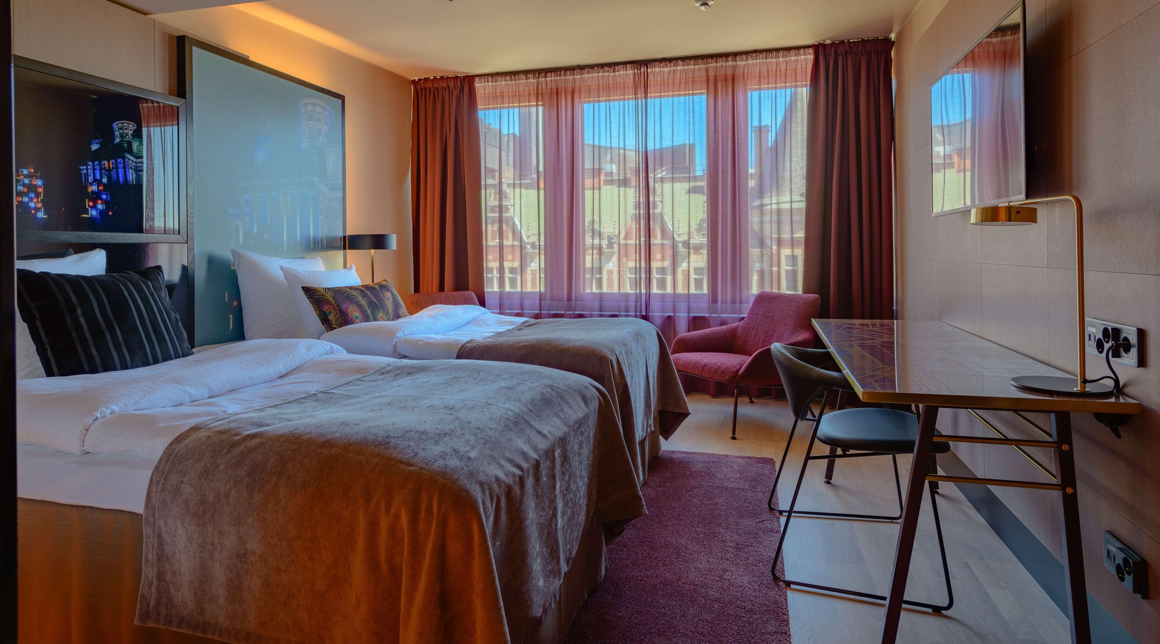 A hotel room with two beds, a desk, a chair, and a TV.