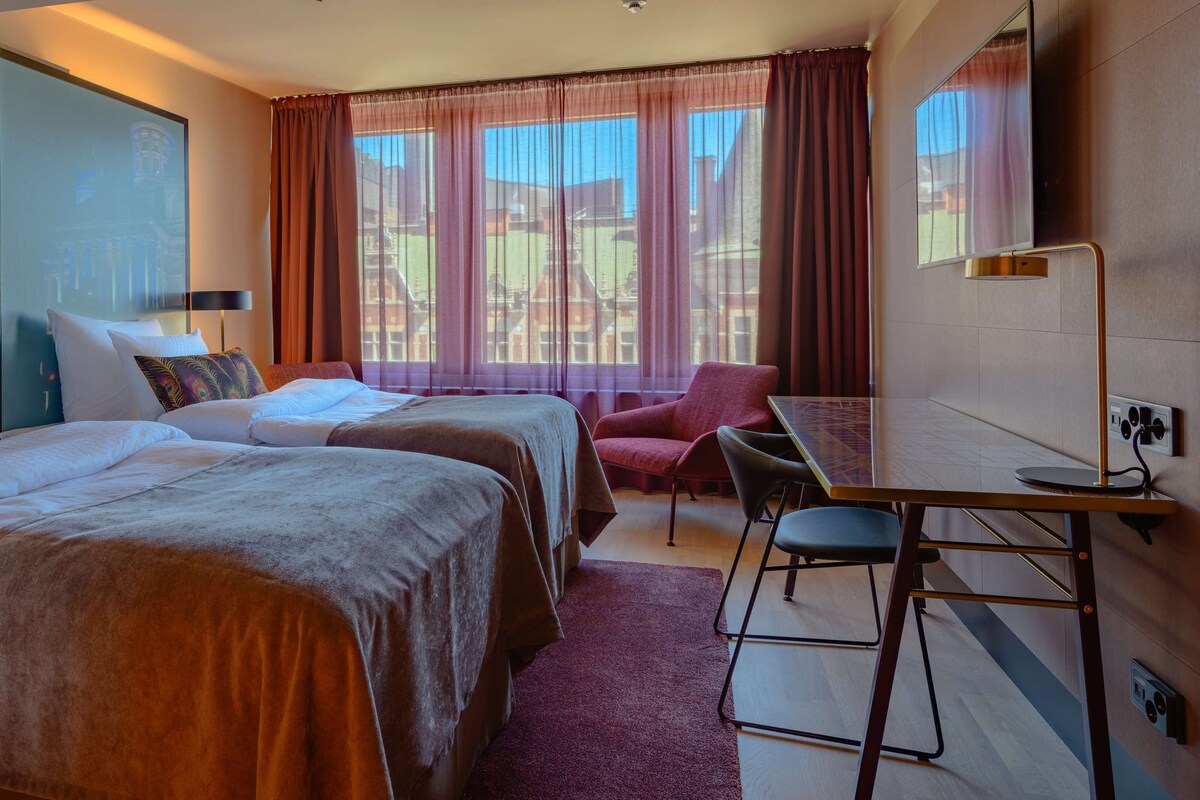 Habitación de hotel con dos camas, un escritorio, una silla y un televisor.
